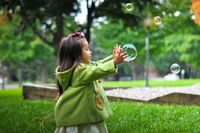 Baby girl bursting bubbles in a park