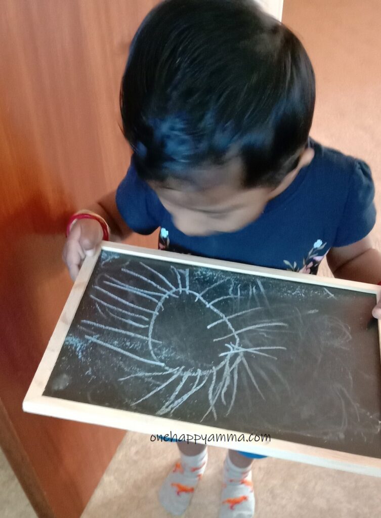 Toddler drawing on a board with a chalk for fun indoor activities to do with toddlers on One Happy Amma